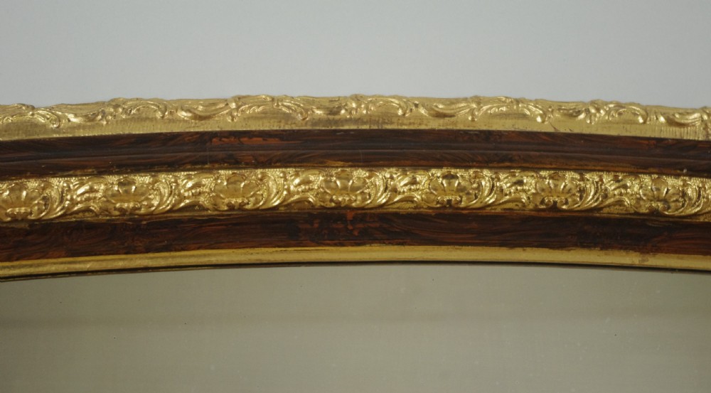 A large Victorian arched overmantel mirror featuring a simulated dark wood frame with detailed parcel-gilt foliage moulding along the inner and outer borders. View VI