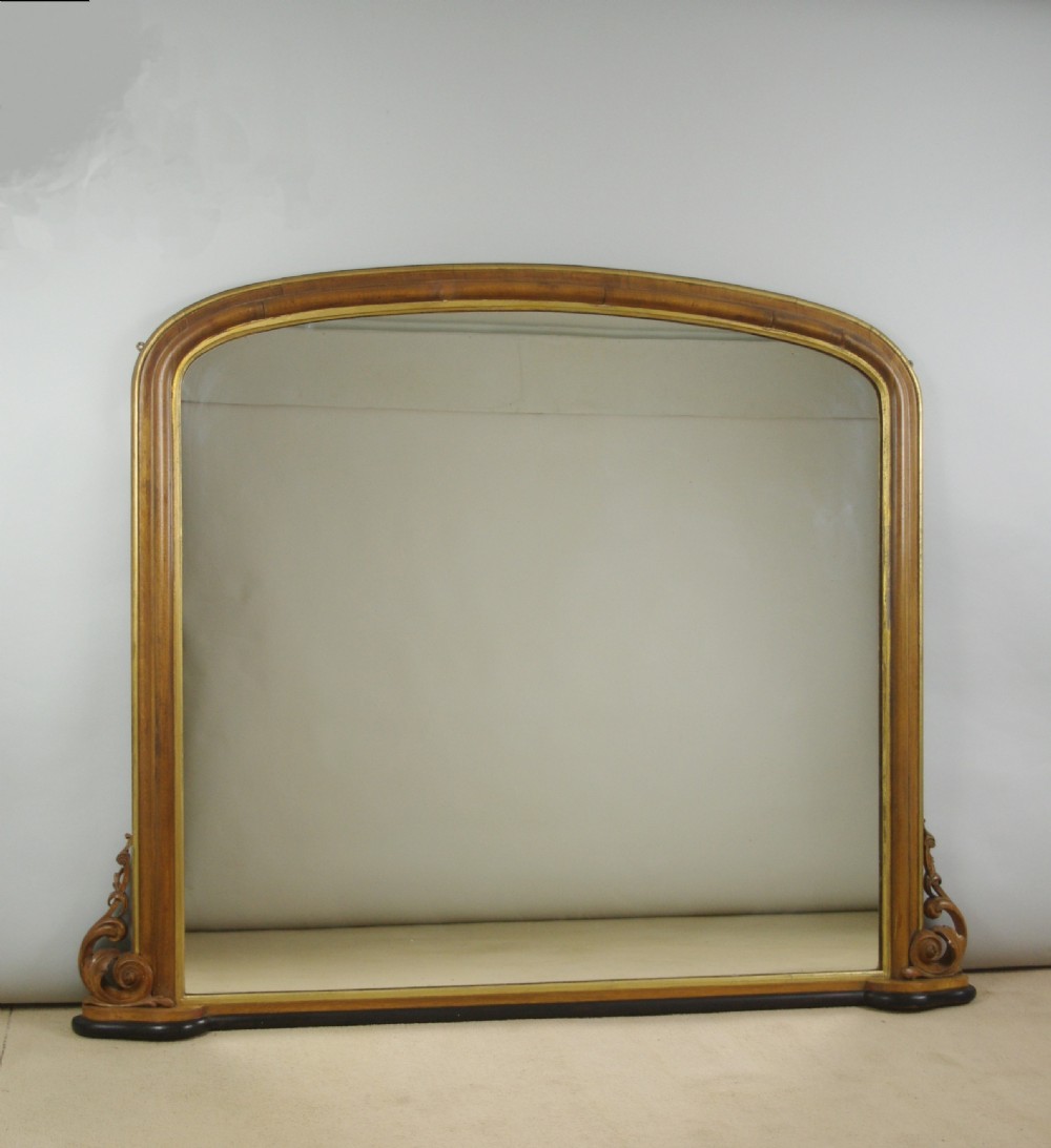 A large Victorian arch-top overmantel mirror with a moulded oak frame, parcel-gilt inner rim, and carved scroll bases.