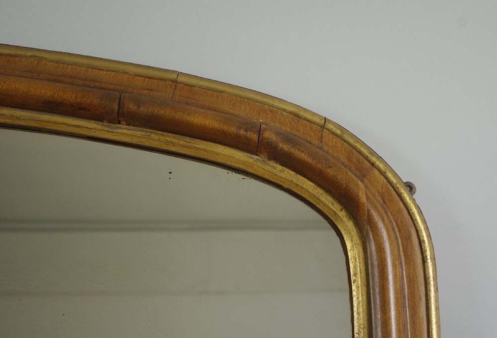 A large Victorian arch-top overmantel mirror with a moulded oak frame, parcel-gilt inner rim, and carved scroll bases. View VI