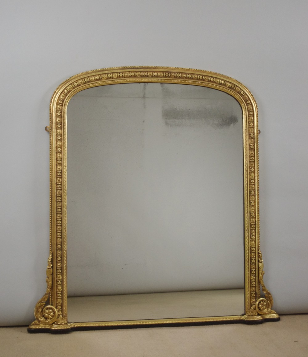 A Victorian giltwood overmantel mirror featuring an arched top frame, beaded relief moulding, and decorative scrollwork supports at the base.