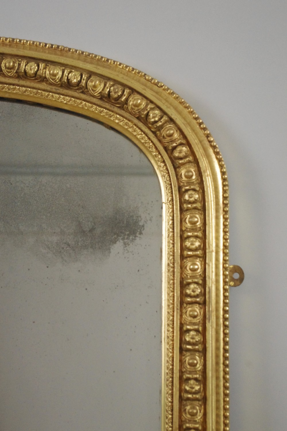A Victorian giltwood overmantel mirror featuring an arched top frame, beaded relief moulding, and decorative scrollwork supports at the base. View IV