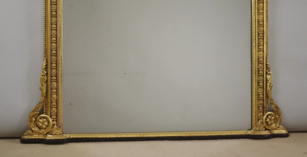 A Victorian giltwood overmantel mirror featuring an arched top frame, beaded relief moulding, and decorative scrollwork supports at the base. View VII