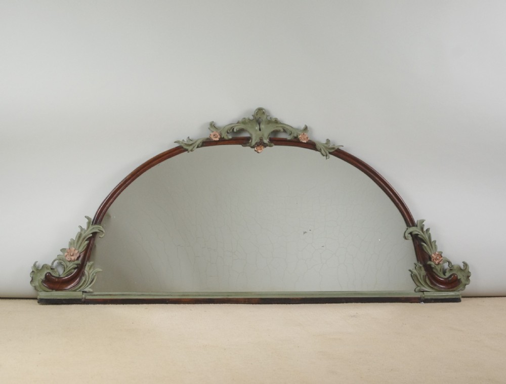A Victorian arch-top mahogany overmantel mirror with carved sage green scrolling foliage and pale pink painted flowers around the frame.