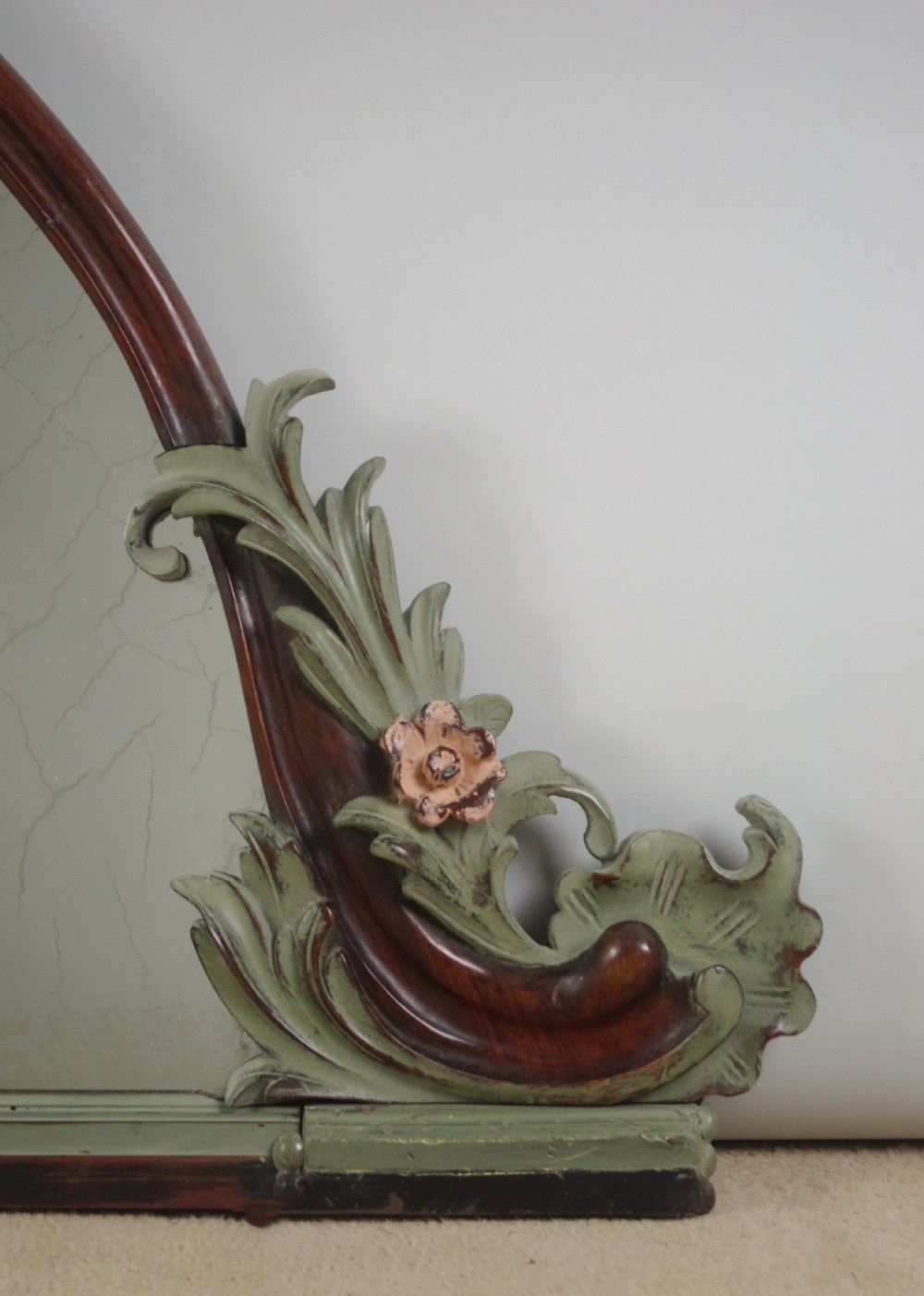 A Victorian arch-top mahogany overmantel mirror with carved sage green scrolling foliage and pale pink painted flowers around the frame. View V