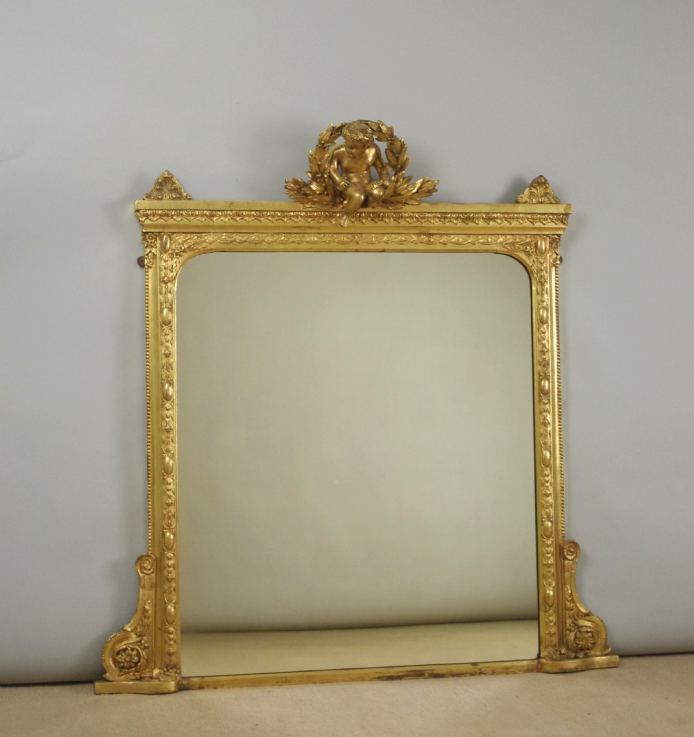 A 19th-century Victorian giltwood overmantel mirror featuring a moulded arch frame decorated with bead moulding and topped with a sculpted putto cresting within a laurel wreath.