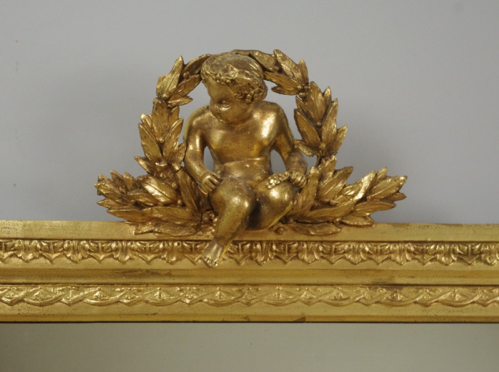 A 19th-century Victorian giltwood overmantel mirror featuring a moulded arch frame decorated with bead moulding and topped with a sculpted putto cresting within a laurel wreath. View III