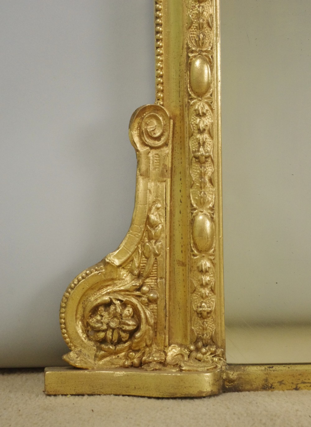 A 19th-century Victorian giltwood overmantel mirror featuring a moulded arch frame decorated with bead moulding and topped with a sculpted putto cresting within a laurel wreath. View VI