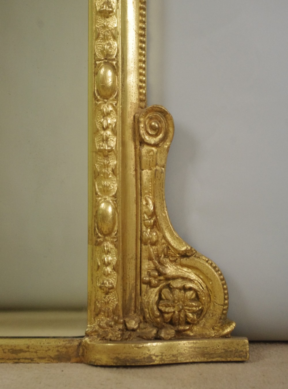 A 19th-century Victorian giltwood overmantel mirror featuring a moulded arch frame decorated with bead moulding and topped with a sculpted putto cresting within a laurel wreath. View VII
