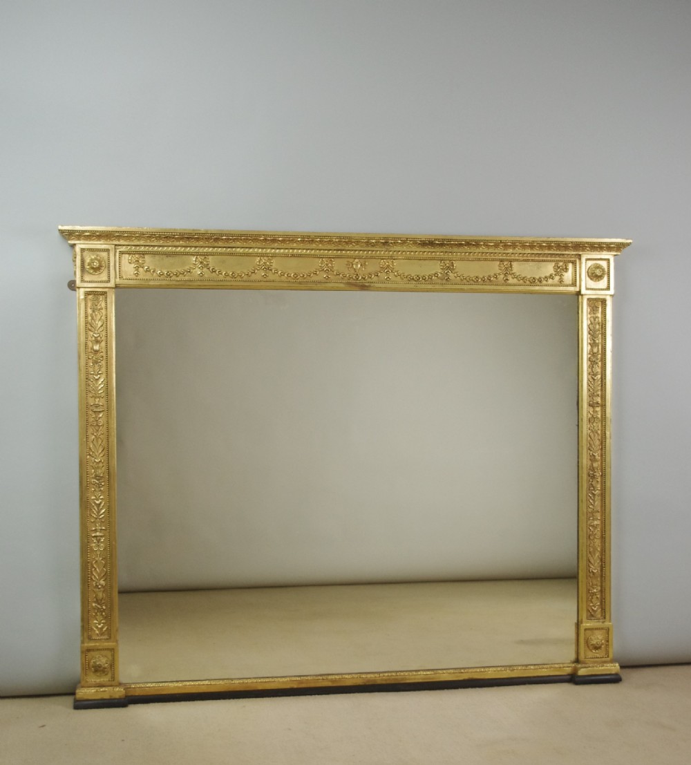 A large rectangular Victorian gilt overmantel mirror featuring Neoclassical swags, rosettes, and beaded moulding along the frame.