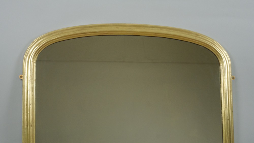 A Victorian arched overmantel mirror featuring a moulded gold-leaf frame with carved scroll flourishes at the lower corners. View II