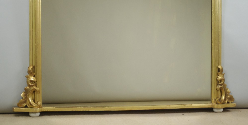 A Victorian arched overmantel mirror featuring a moulded gold-leaf frame with carved scroll flourishes at the lower corners. View VIII