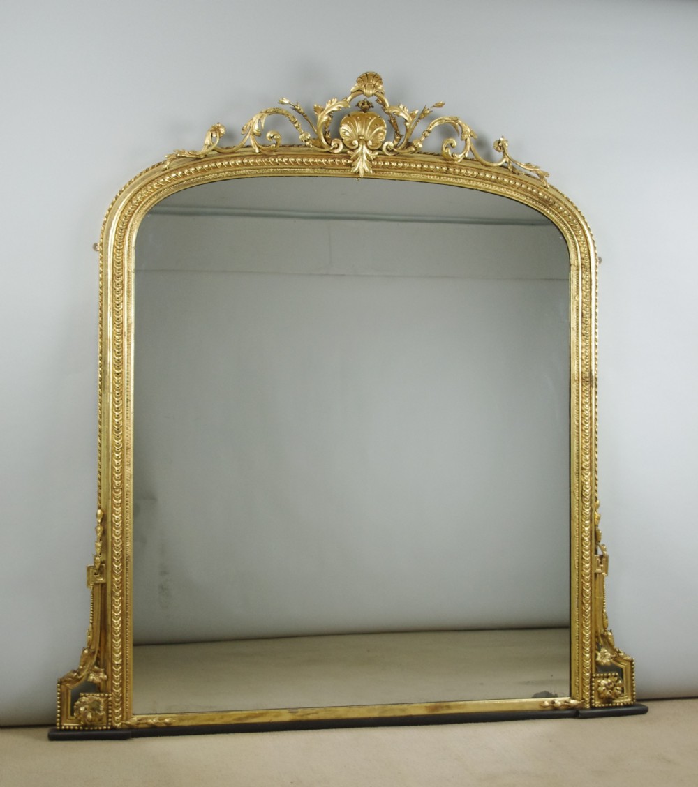 A large Victorian giltwood overmantel mirror featuring an arched top frame topped with an elaborate carved shell cresting.
