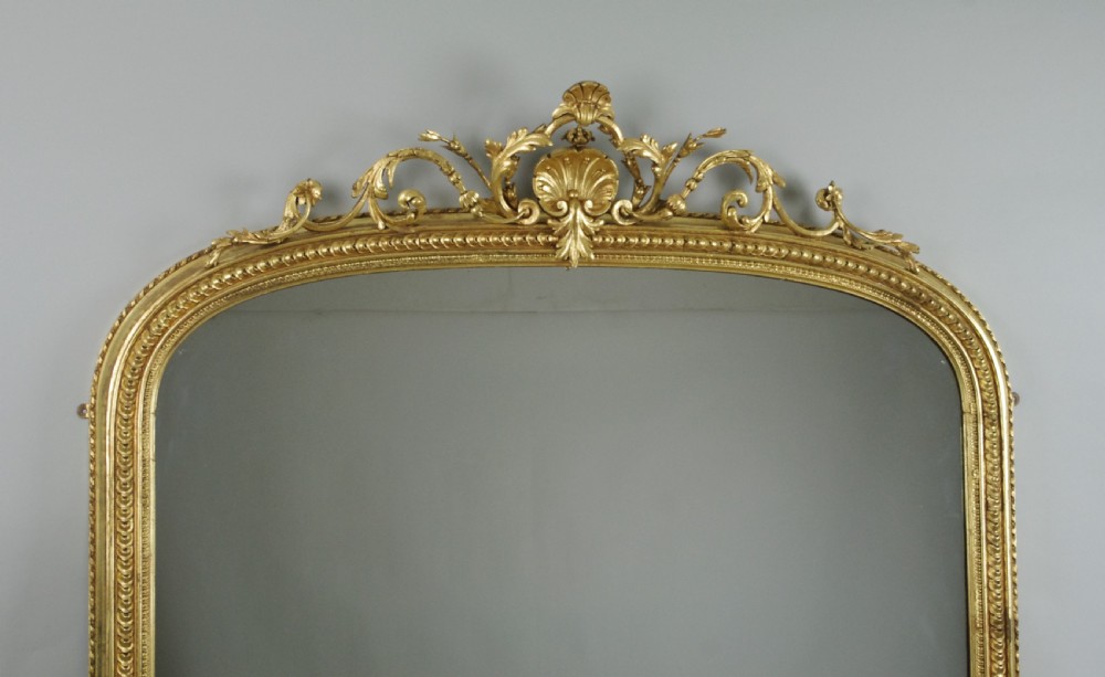 A large Victorian giltwood overmantel mirror featuring an arched top frame topped with an elaborate carved shell cresting. View II