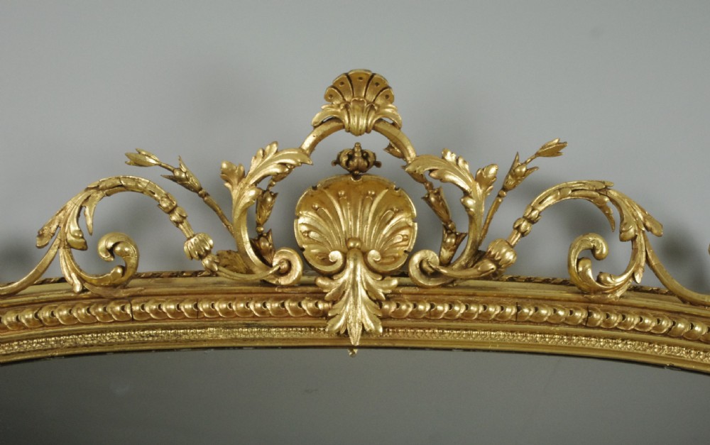 A large Victorian giltwood overmantel mirror featuring an arched top frame topped with an elaborate carved shell cresting. View III
