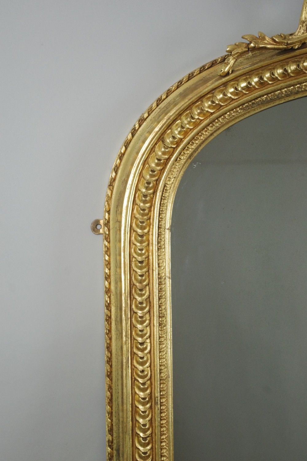 A large Victorian giltwood overmantel mirror featuring an arched top frame topped with an elaborate carved shell cresting. View V