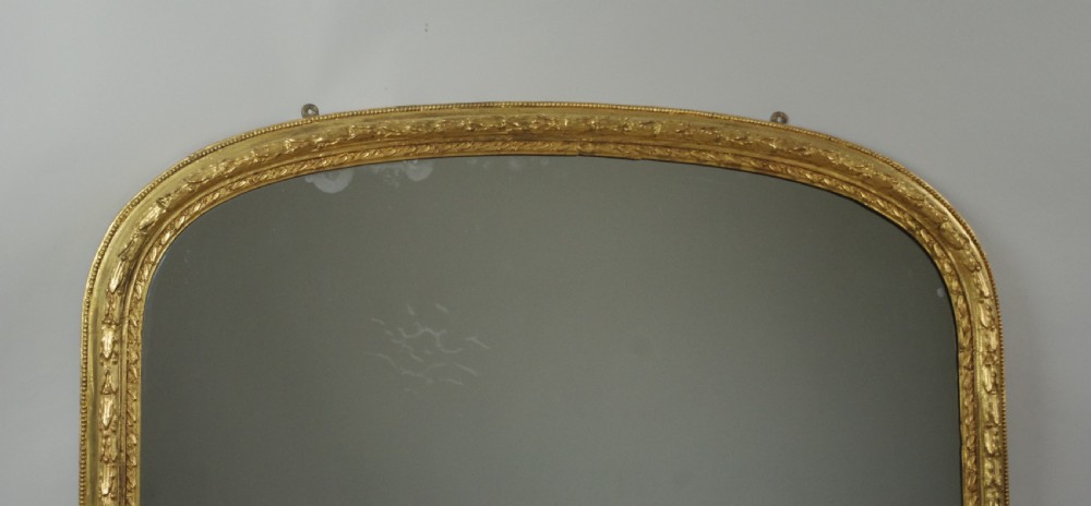 A large Victorian arched overmantel mirror featuring a gold giltwood frame with leaf moulding and a flat base. View II