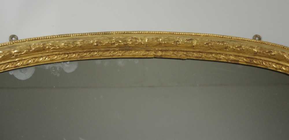 A large Victorian arched overmantel mirror featuring a gold giltwood frame with leaf moulding and a flat base. View IX