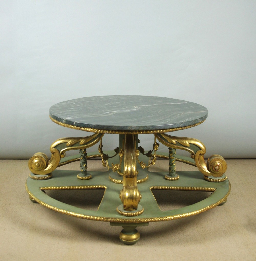 A low circular French Neoclassical style centre table featuring a dark green marble top and a sage green painted base with carved parcel-gilt scroll supports.