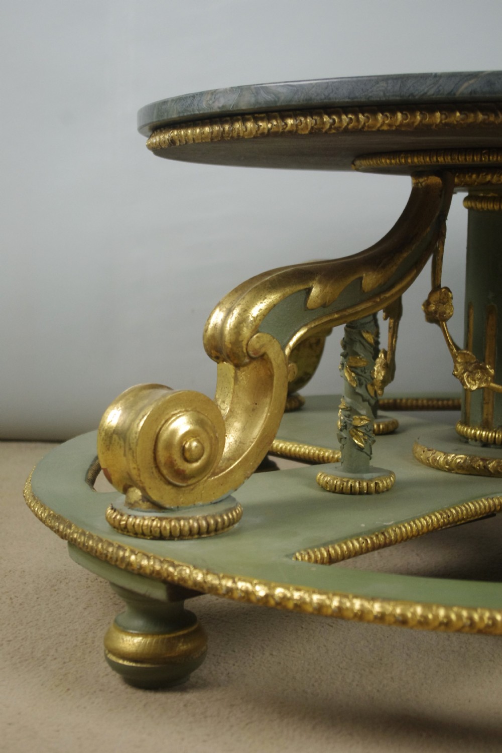 A low circular French Neoclassical style centre table featuring a dark green marble top and a sage green painted base with carved parcel-gilt scroll supports. View V