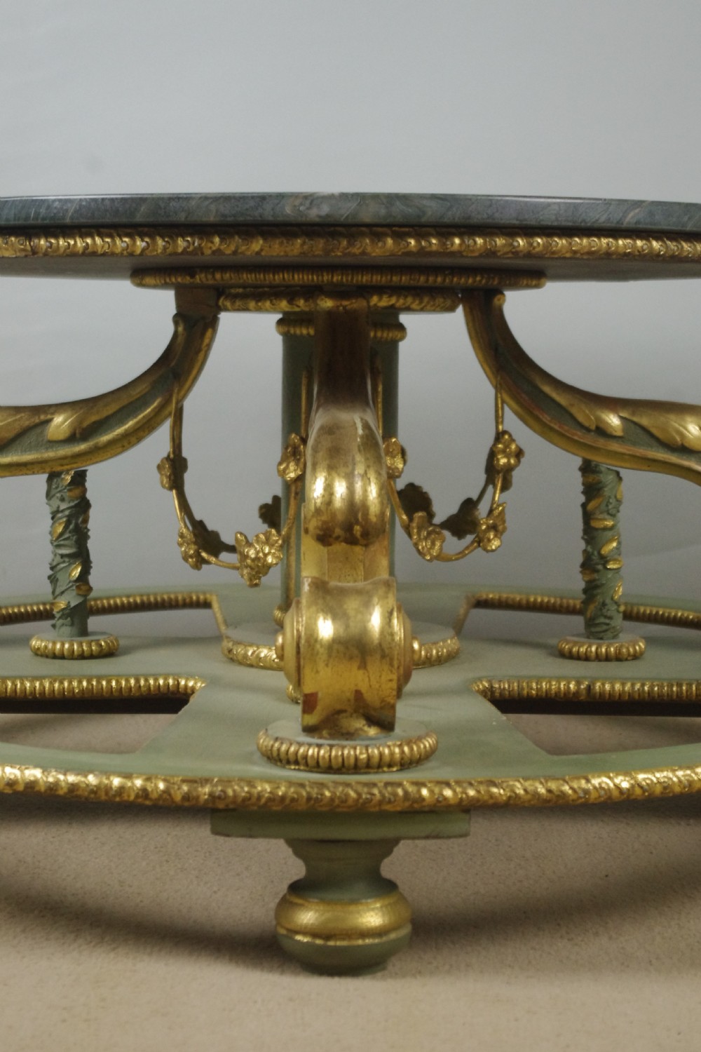 A low circular French Neoclassical style centre table featuring a dark green marble top and a sage green painted base with carved parcel-gilt scroll supports. View VI