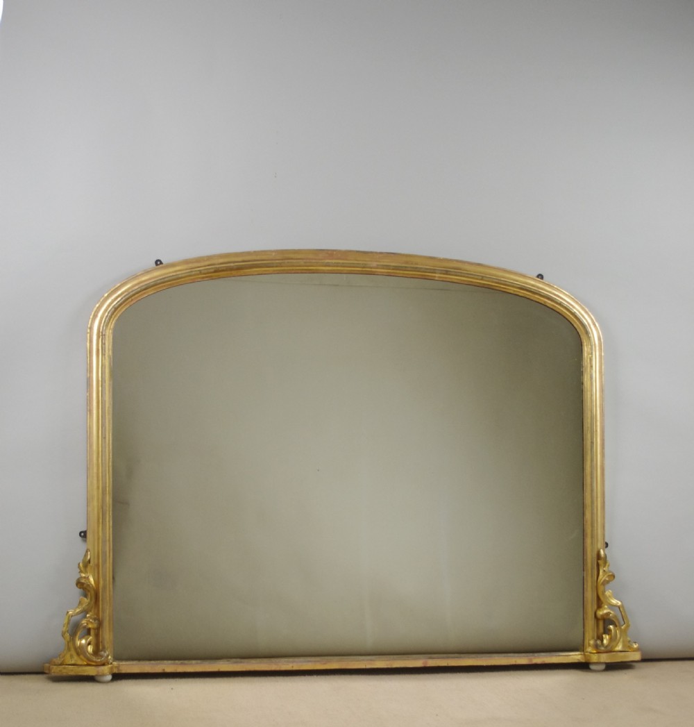 A large Victorian arched overmantel mirror featuring a gilded wood frame with decorative scroll side corbels.