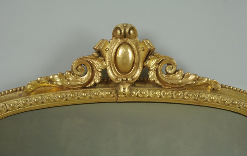 A Victorian giltwood overmantel mirror featuring an arched top decorated with a central crest motif, beaded trim moulding, and side scrolls. View III
