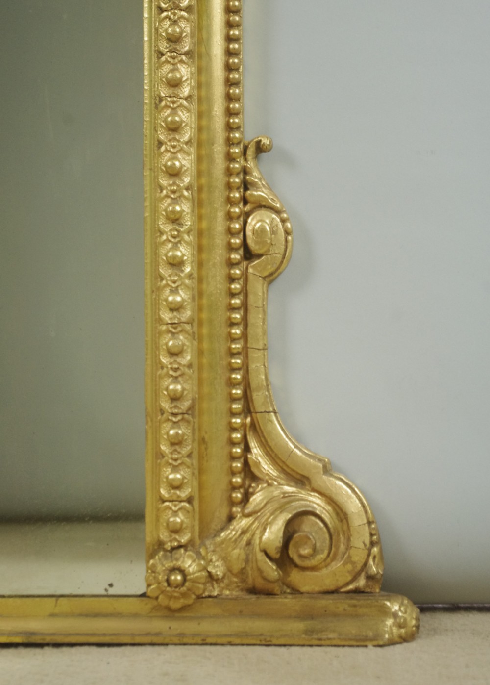A Victorian giltwood overmantel mirror featuring an arched top decorated with a central crest motif, beaded trim moulding, and side scrolls. View VIII