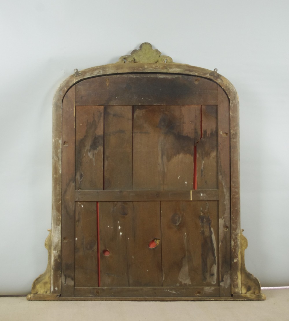 A Victorian giltwood overmantel mirror featuring an arched top decorated with a central crest motif, beaded trim moulding, and side scrolls. View X