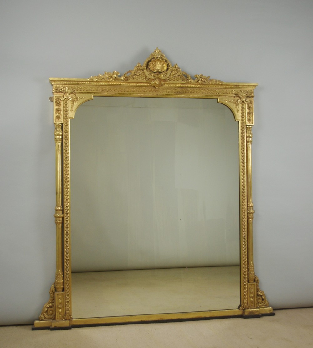 A large Victorian gold gilded overmantel mirror featuring an ornate shell crest pediment and slender side columns.
