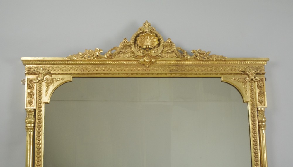A large Victorian gold gilded overmantel mirror featuring an ornate shell crest pediment and slender side columns. View II