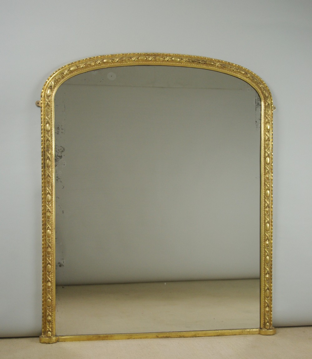 A Victorian arched overmantel mirror featuring a gilded frame with ornate decorative moulding and a flat base.