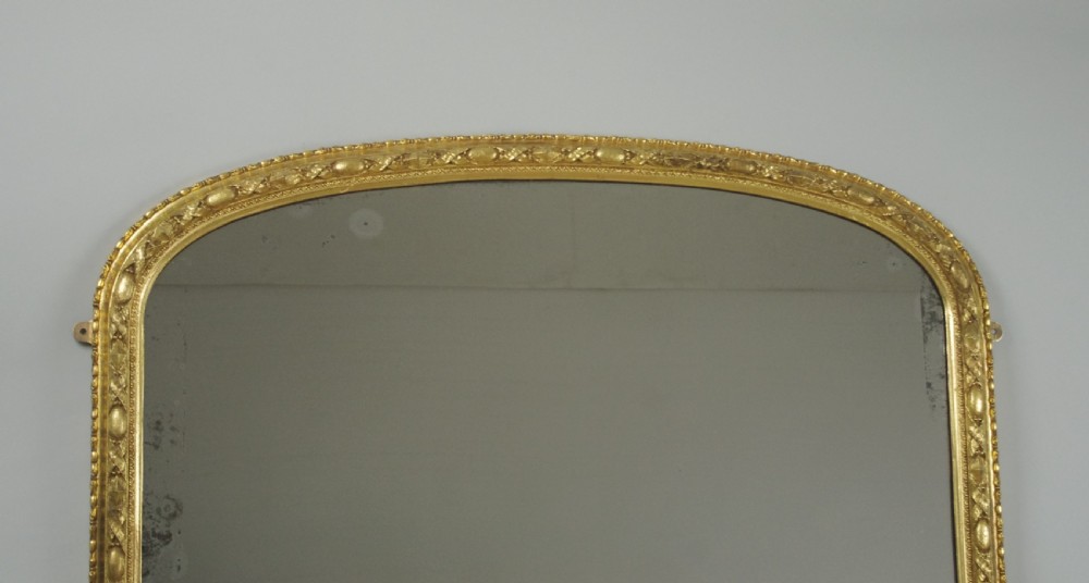 A Victorian arched overmantel mirror featuring a gilded frame with ornate decorative moulding and a flat base. View II