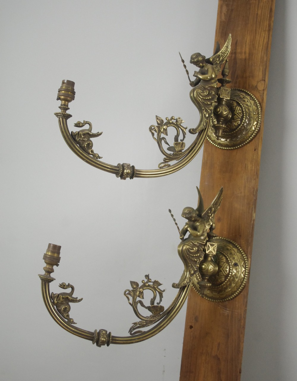 A pair of cast brass Victorian wall sconces featuring sculpted cherubs, mythological creature accents, and ornamental scroll arms.