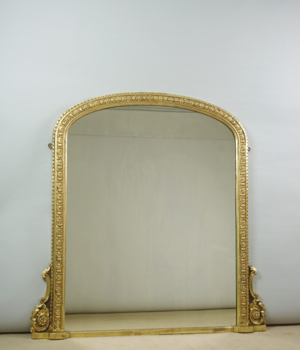 A large Victorian giltwood overmantel mirror featuring an arched top frame with moulded detailing and decorative scrolled side supports.