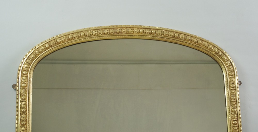 A large Victorian giltwood overmantel mirror featuring an arched top frame with moulded detailing and decorative scrolled side supports. View II