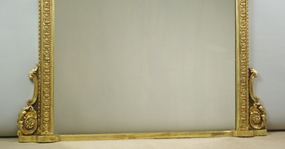 A large Victorian giltwood overmantel mirror featuring an arched top frame with moulded detailing and decorative scrolled side supports. View VII