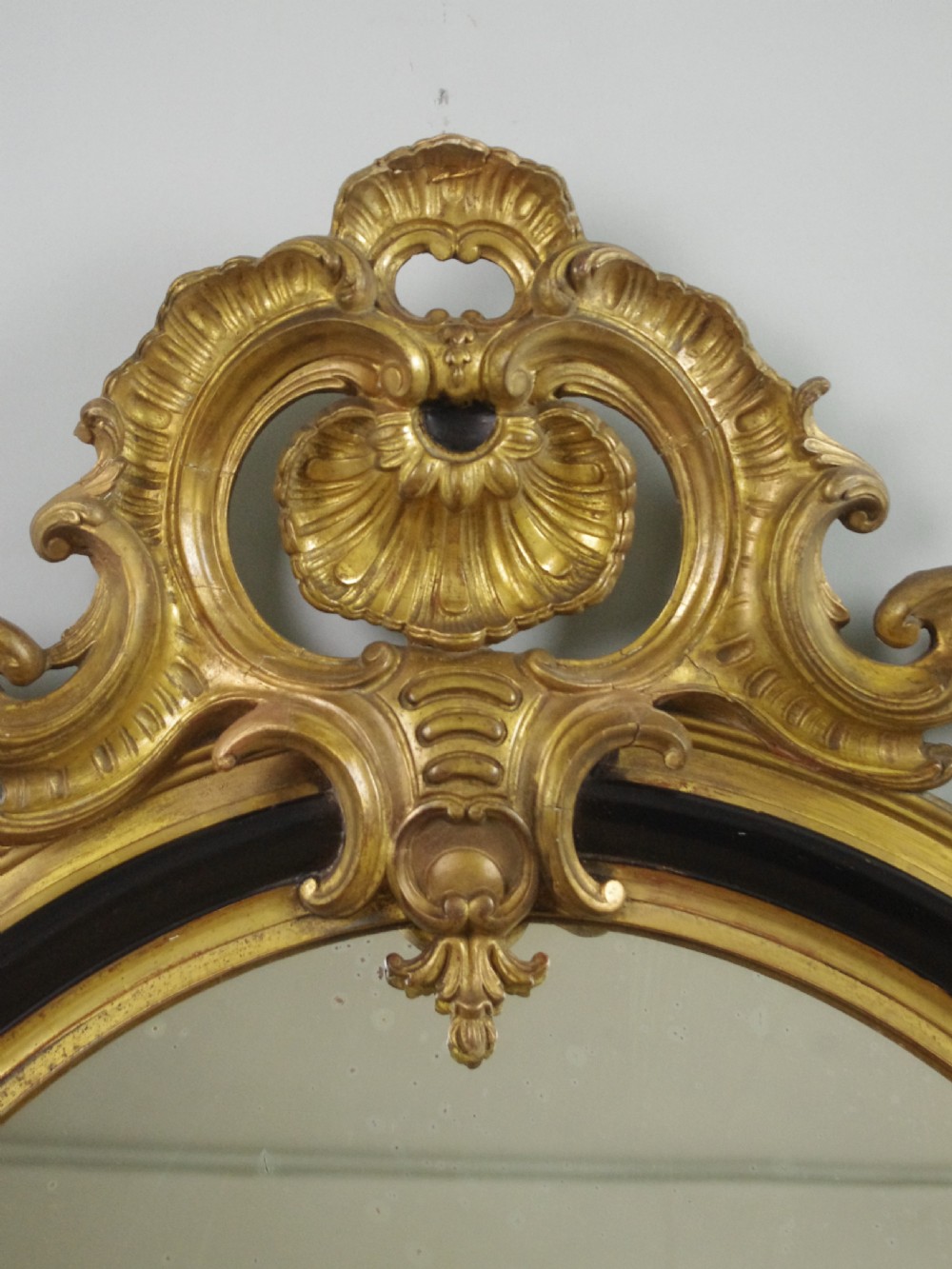 A nineteenth-century French oval wall mirror featuring an ebonised and parcel-gilt frame with a carved shell pediment crest. View III