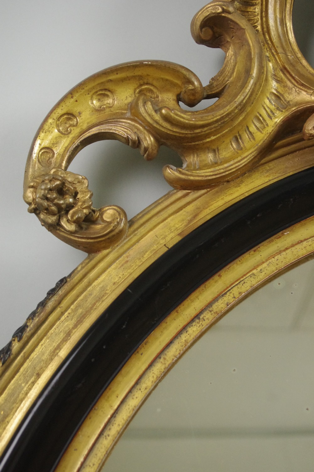 A nineteenth-century French oval wall mirror featuring an ebonised and parcel-gilt frame with a carved shell pediment crest. View V