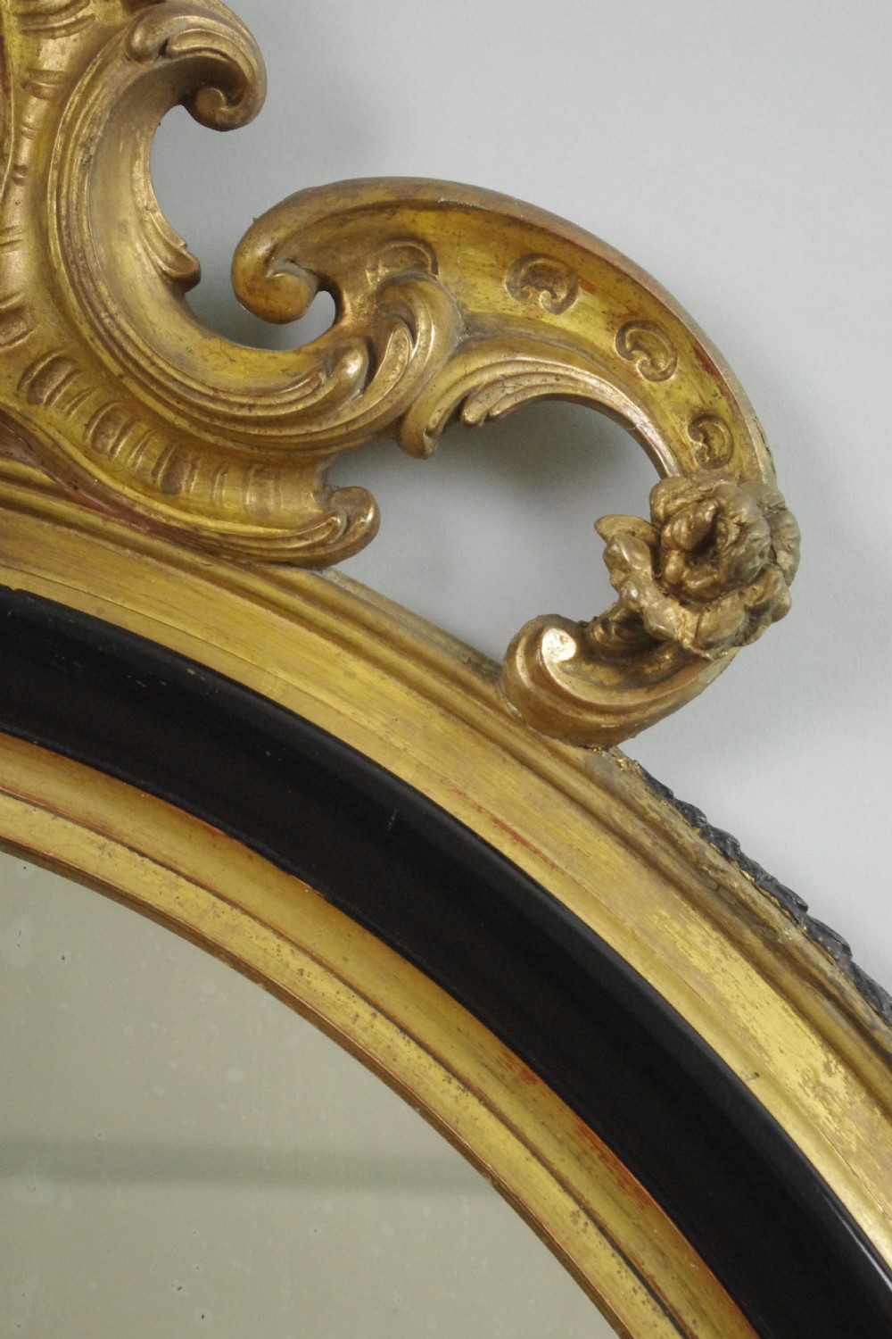 A nineteenth-century French oval wall mirror featuring an ebonised and parcel-gilt frame with a carved shell pediment crest. View VI