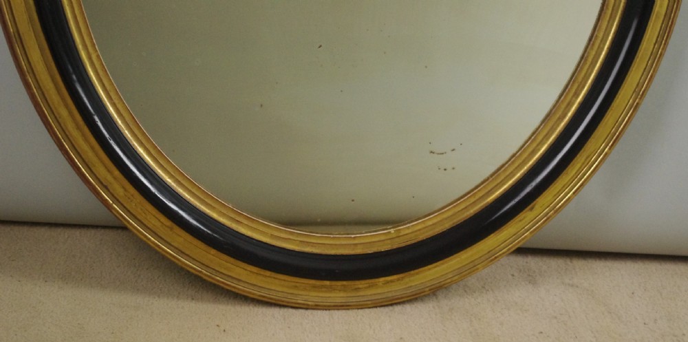 A nineteenth-century French oval wall mirror featuring an ebonised and parcel-gilt frame with a carved shell pediment crest. View VII