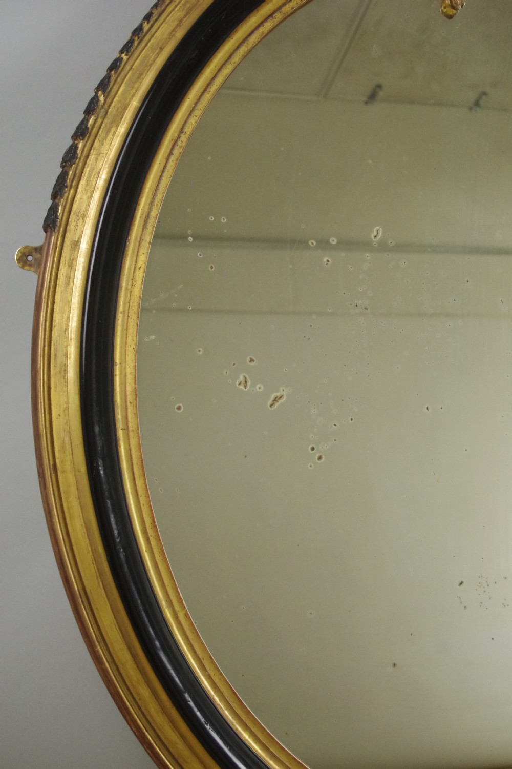 A nineteenth-century French oval wall mirror featuring an ebonised and parcel-gilt frame with a carved shell pediment crest. View VIII