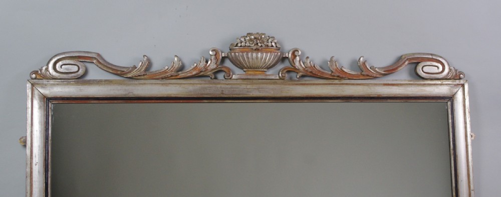 A large Victorian silvered overmantel mirror featuring a carved central urn cresting, foliate top border, and scrolled bottom corners. View IV