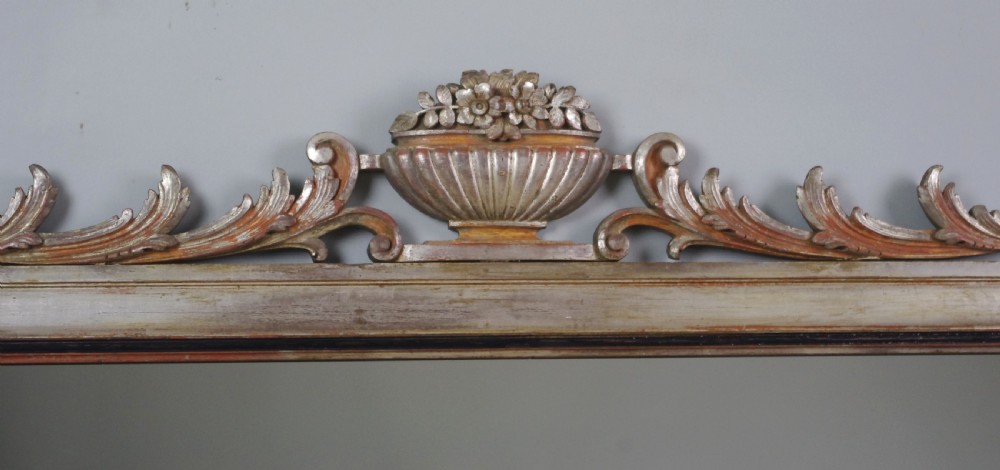 A large Victorian silvered overmantel mirror featuring a carved central urn cresting, foliate top border, and scrolled bottom corners. View V