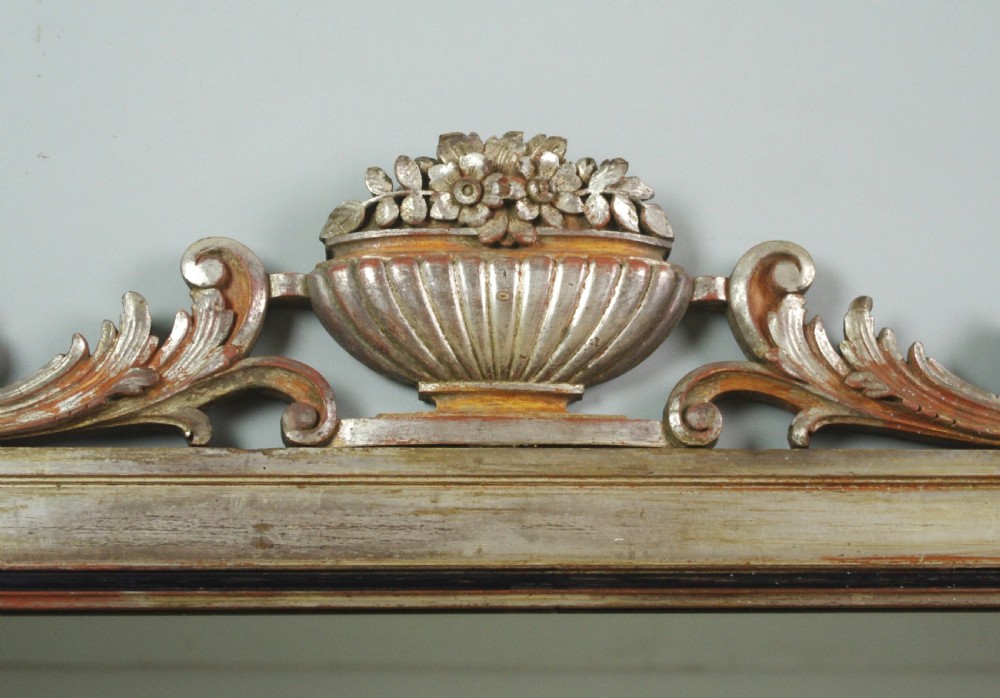 A large Victorian silvered overmantel mirror featuring a carved central urn cresting, foliate top border, and scrolled bottom corners. View VI