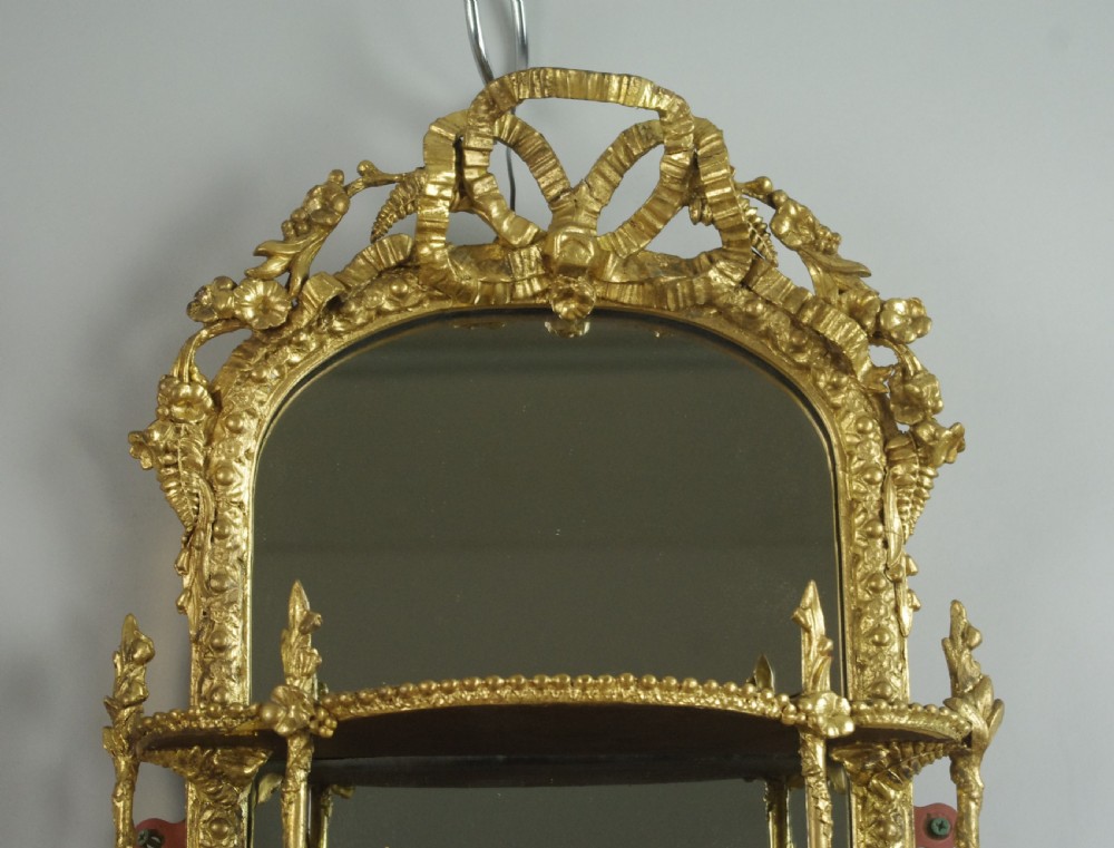 A matching pair of Victorian giltwood wall shelves featuring mirrored backs, ornate bow cresting, and open tiers for displaying small objects. View VI