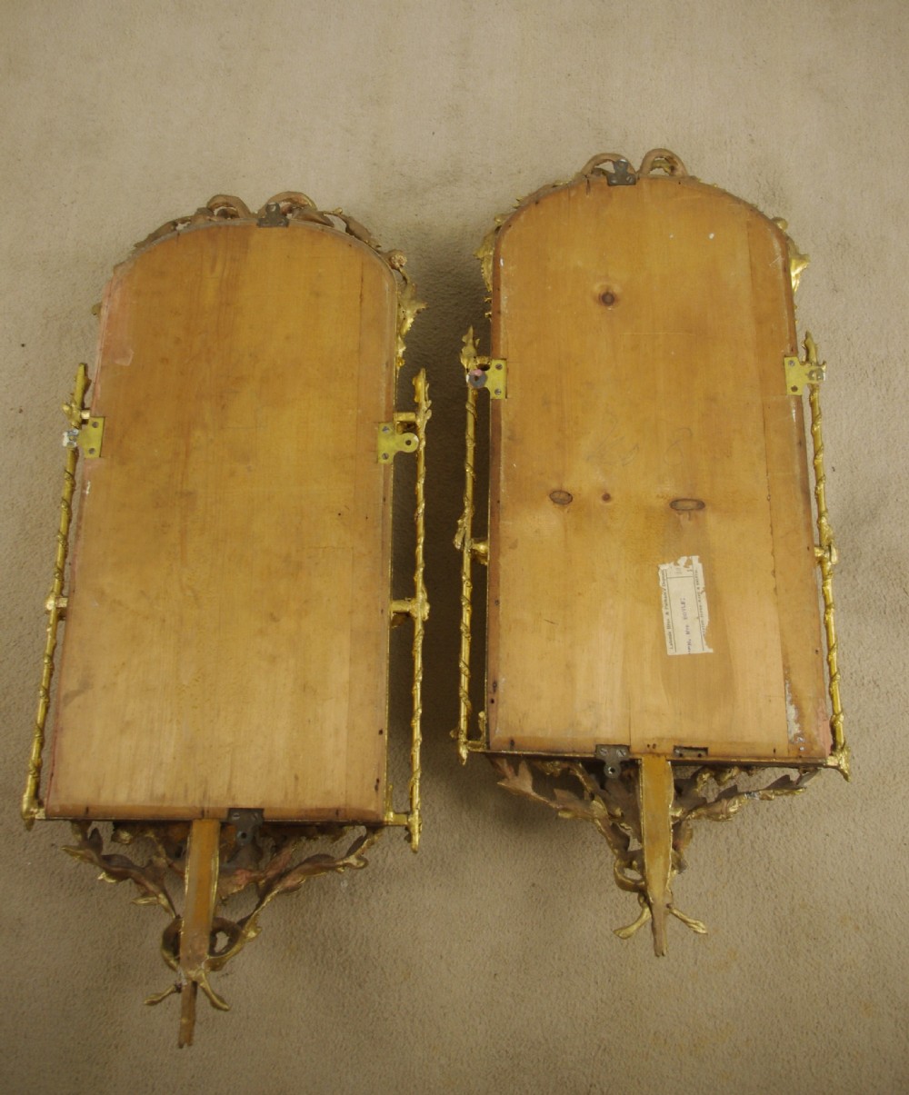 A matching pair of Victorian giltwood wall shelves featuring mirrored backs, ornate bow cresting, and open tiers for displaying small objects. View XV