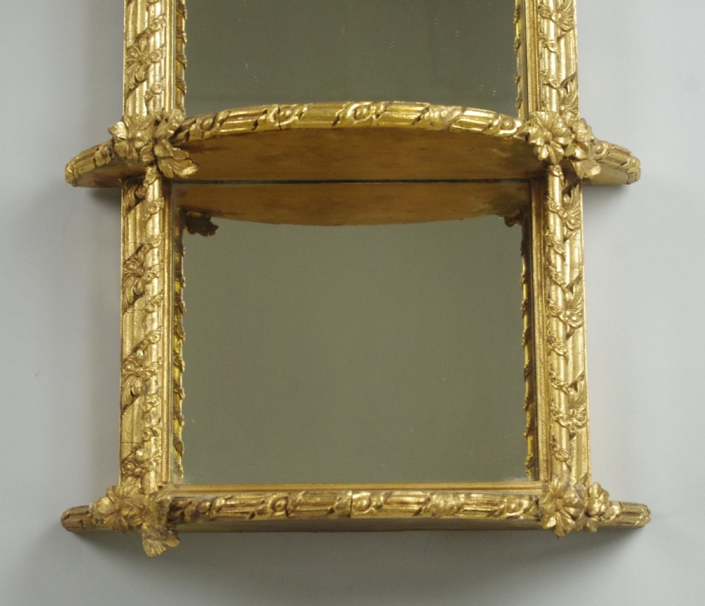 A pair of matching Victorian arched gilt wall mirrors featuring integrated display shelves and ornate moulded frames against a plain background. View VII