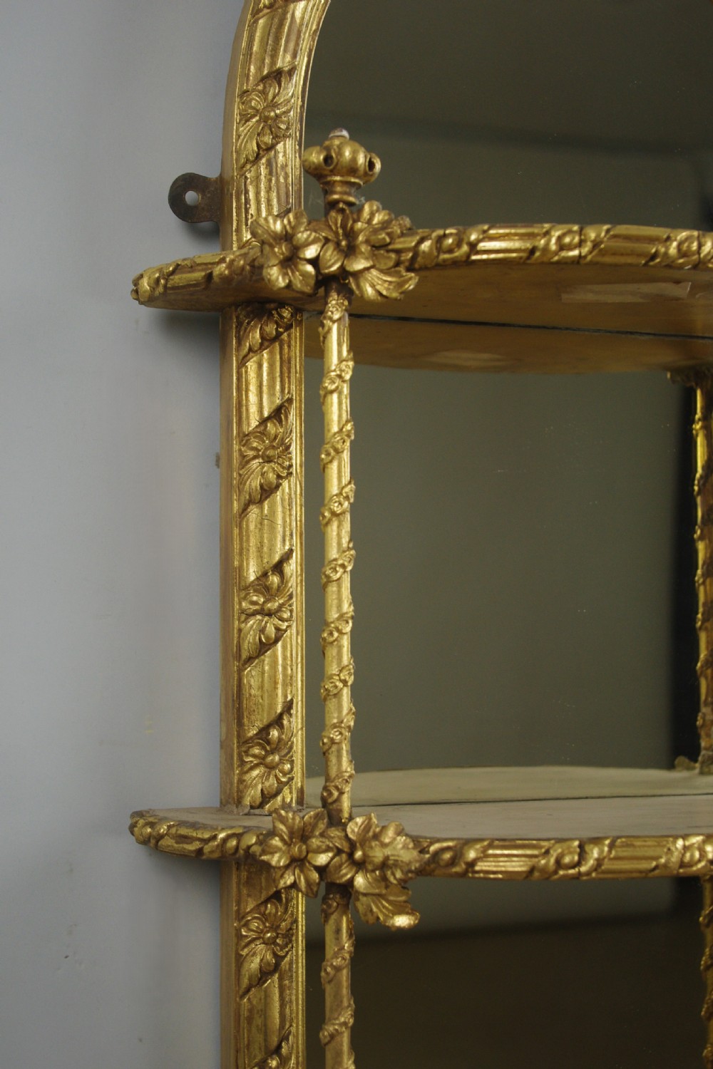 A pair of matching Victorian arched gilt wall mirrors featuring integrated display shelves and ornate moulded frames against a plain background. View VIII