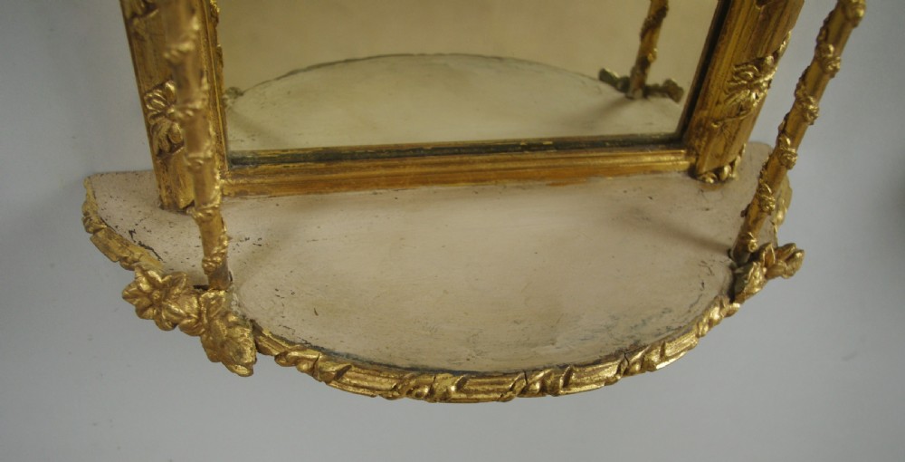 A pair of matching Victorian arched gilt wall mirrors featuring integrated display shelves and ornate moulded frames against a plain background. View XII