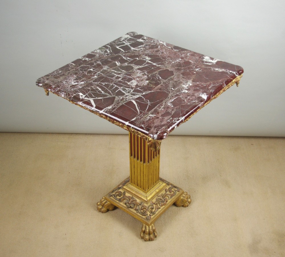 A square Victorian occasional table featuring a red veined marble top resting on a giltwood fluted pedestal with lion paw feet.